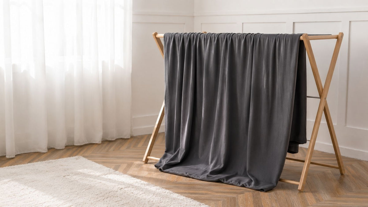 Funda de sofá gris antracita tendida en un tendedero de madera, junto a una ventana