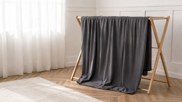 Funda de sofá gris antracita tendida en un tendedero de madera, junto a una ventana